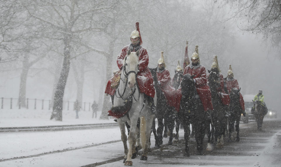 FILE - In this Wednesday, Feb. 28, 2018 file photo members of the Household Cavalry return to their barracks as snow falls in London. Britain, which is buffered by the Atlantic Ocean and tends to have temperate winters, saw heavy snow in some areas that disrupted road, rail and air travel and forced hundreds of schools to close.(AP Photo/Alastair Grant, File)