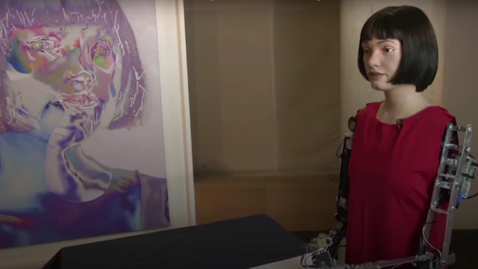 Ai-da, an AI robot, next to one of her self portraits