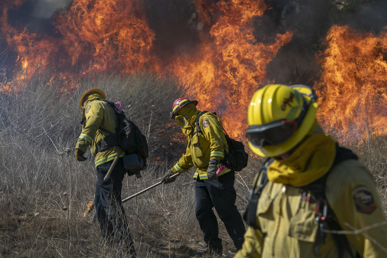 Firefighters in yellow helmets and protective gear set a backfire with wands to protect homes.