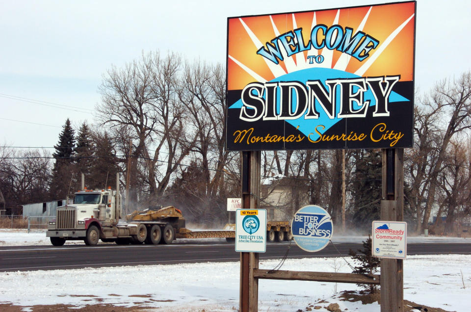 This Feb. 28, 2012 photo shows a truck driving by the welcome sign for Sidney, Mont. Sidney is experiencing a boom spurred by companies seeking to extract oil from the massive Bakken formation beneath western North Dakota and eastern Montana. More than 16 million barrels of crude are now being pumped every month from the massive Bakken oil field beneath eastern Montana. But Sidney's new-found prosperity doesn't dull the sting of the recent kidnapping and apparent murder of a local teacher, Sherry Arnold, who authorities allege was snatched from a Sidney street by two men among the thousands in search of their own slice of the boom's multi-billion-dollar payoff. (AP Photo/Matthew Brown)