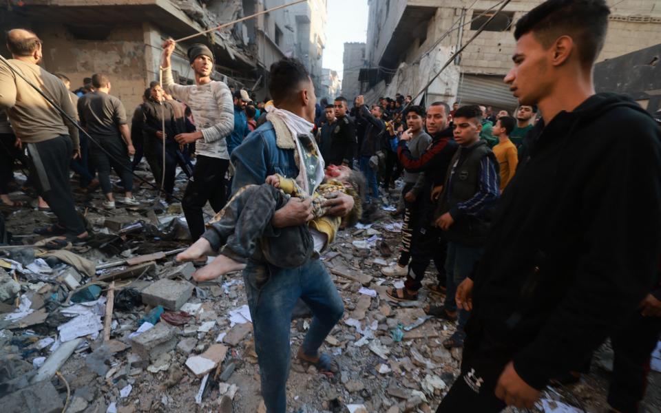 A Palestinian youth carries a badly wounded child as poeple rush out of a bombarded area in the Rafah refugee camp