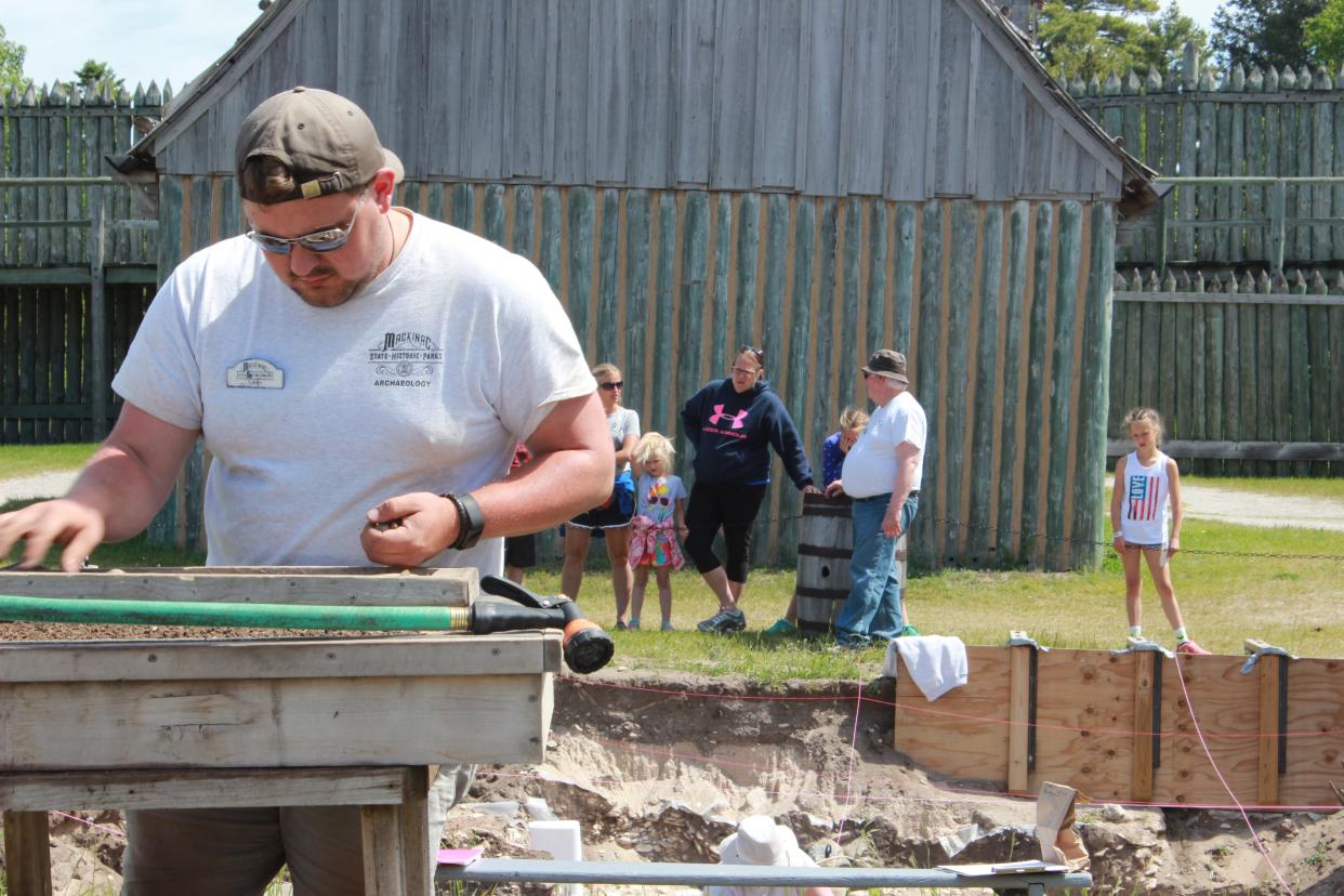 An archaeologist at Colonial Michilimackinac is watched by guests.