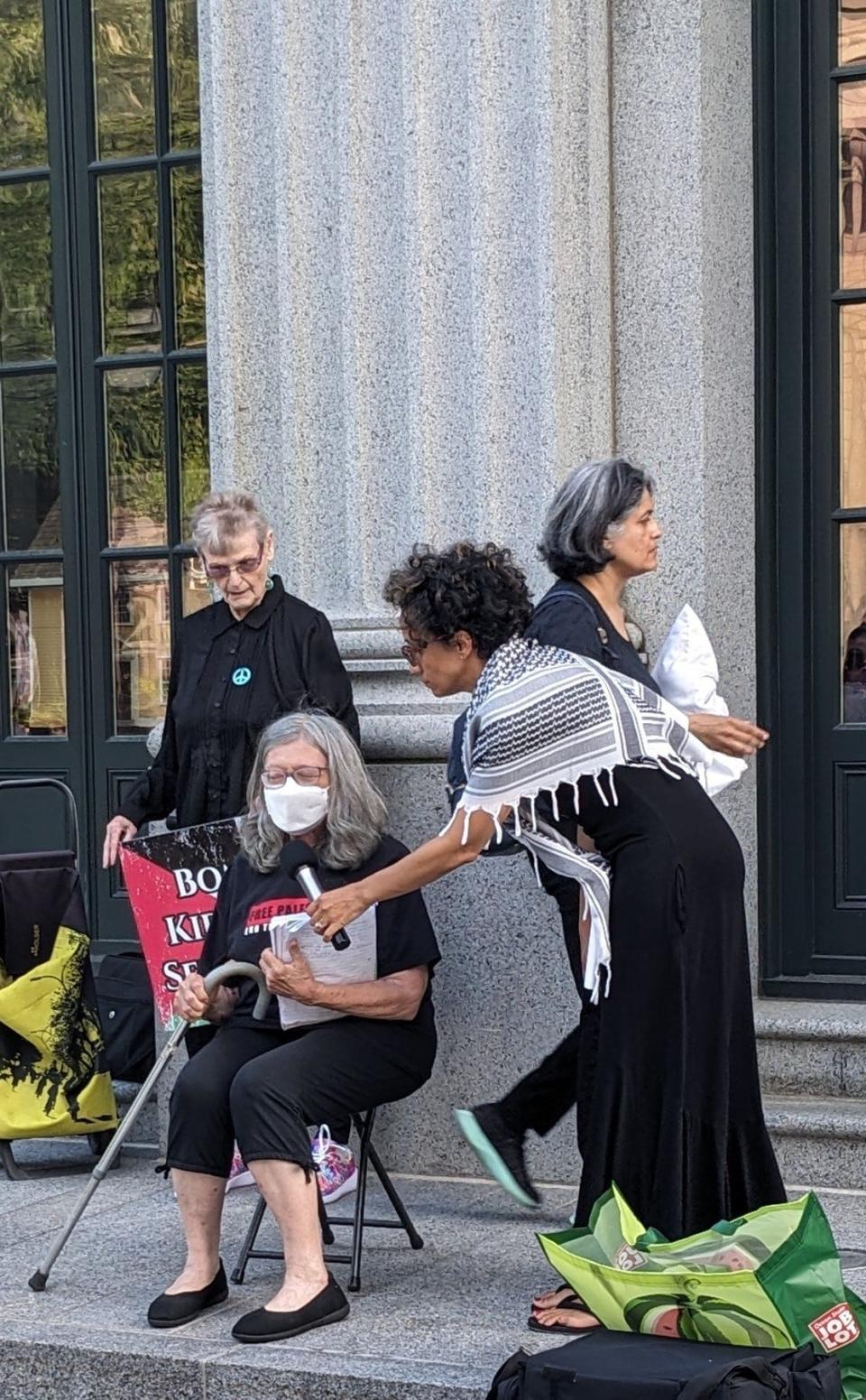 Fay Strigler, seated, assisted by Charisma Henderson, speaks at a vigil held in Quincy Center for Palestinian victims of Israeli military operations in Gaza.