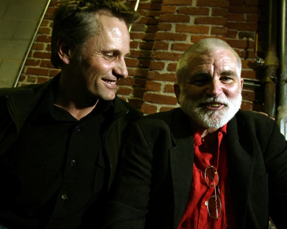 Mike Davis, in a red shirt and blazer, smiles as Viggo Mortensen looks on.