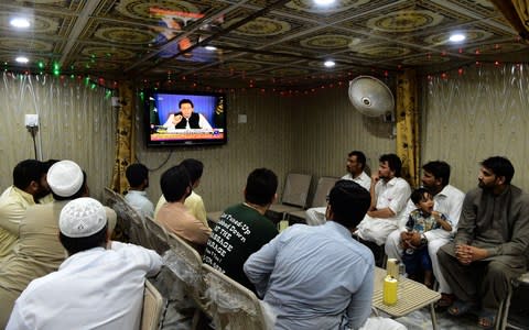 Pakistani men watch a television broadcasting Imran Khan's speech - Credit: ABDUL MAJEED/AFP