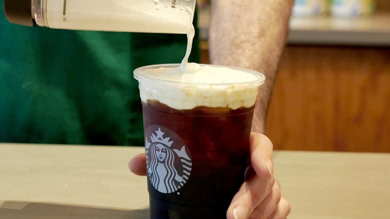 Barista pouring cold foam onto an iced Starbucks drink