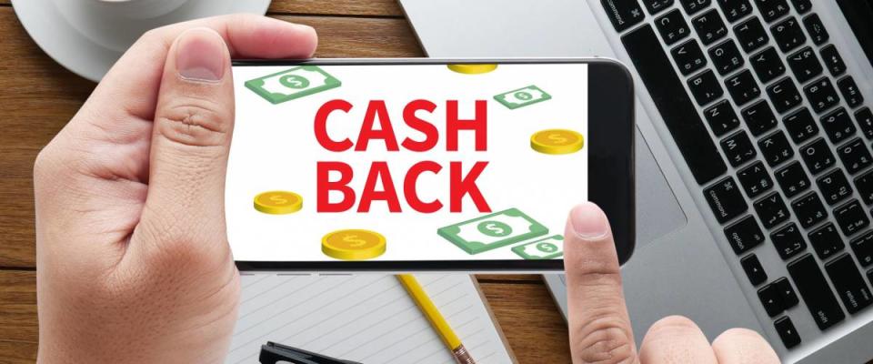 CASH BACK message on hand holding to touch a phone, top view, table computer coffee and book