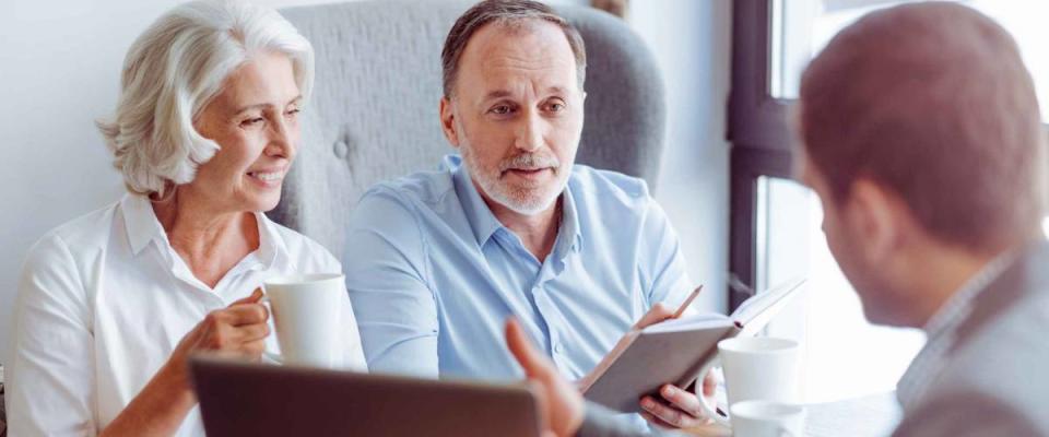 Happy older couple sits across table from man in office