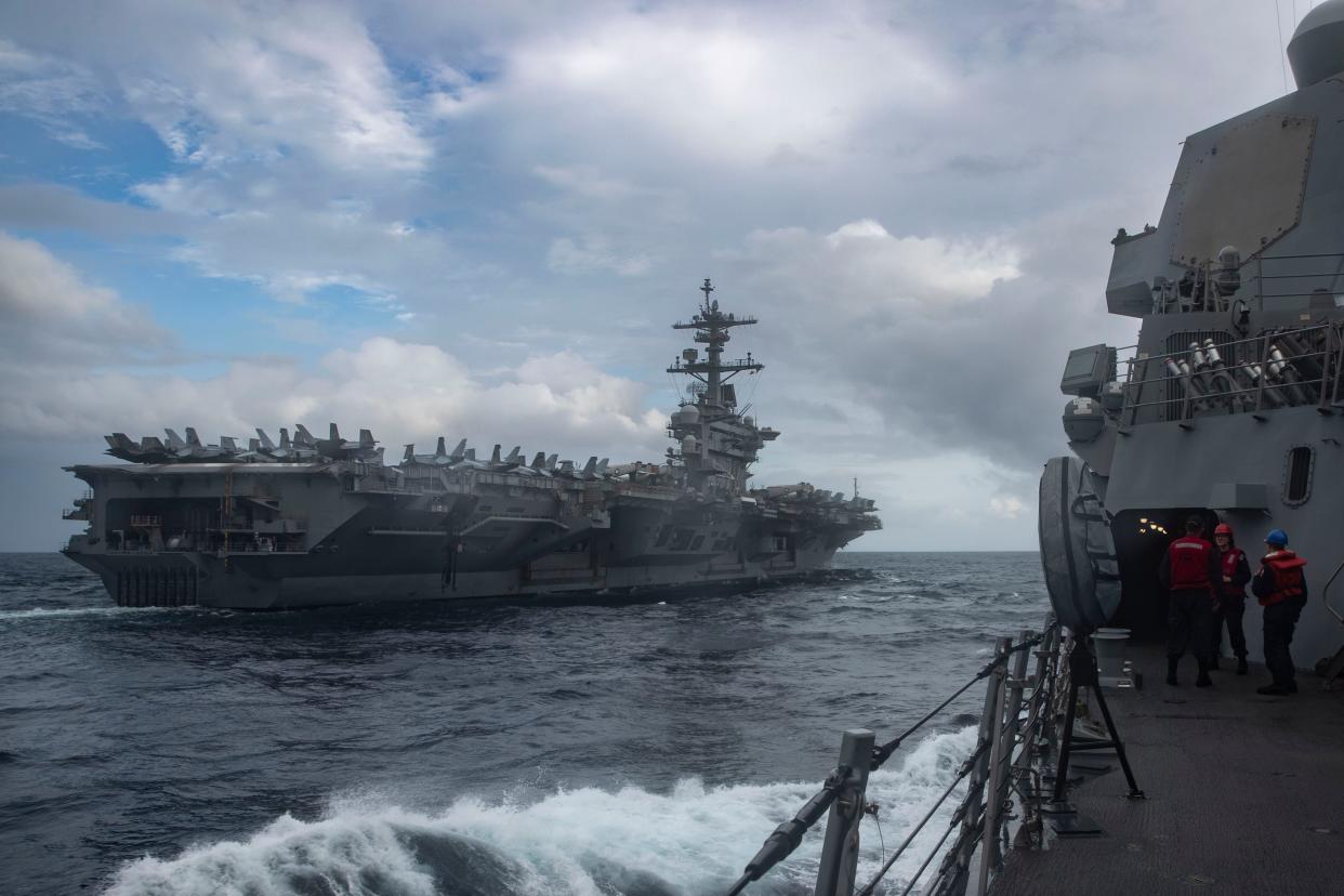 A view from aboard the US Navy destroyer USS Frank E. Petersen Jr. of the aircraft carrier USS Abraham Lincoln sailing on the open ocean.