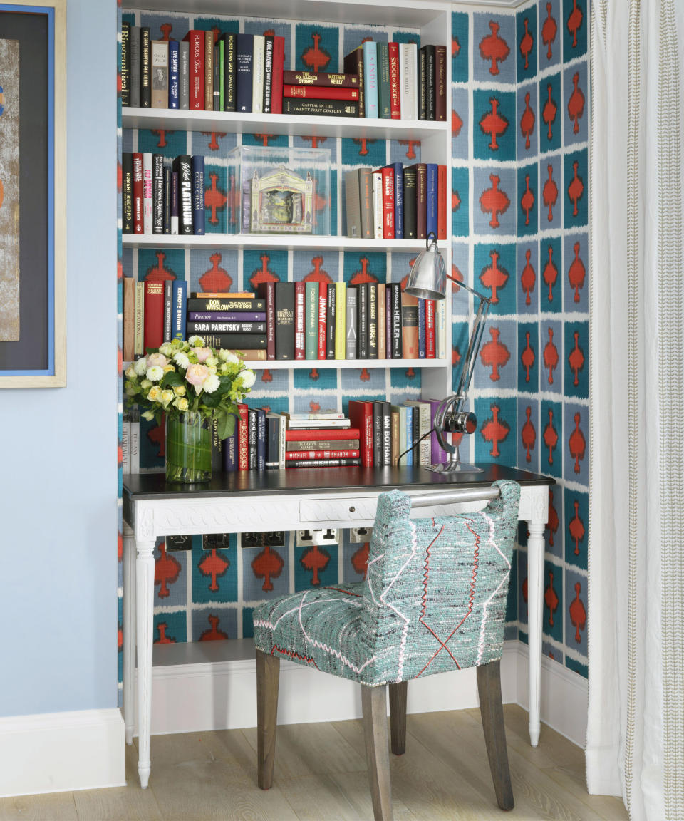 Colorful nook decorated with blue and red patterned wallpaper, bookshelf, small desk and chair