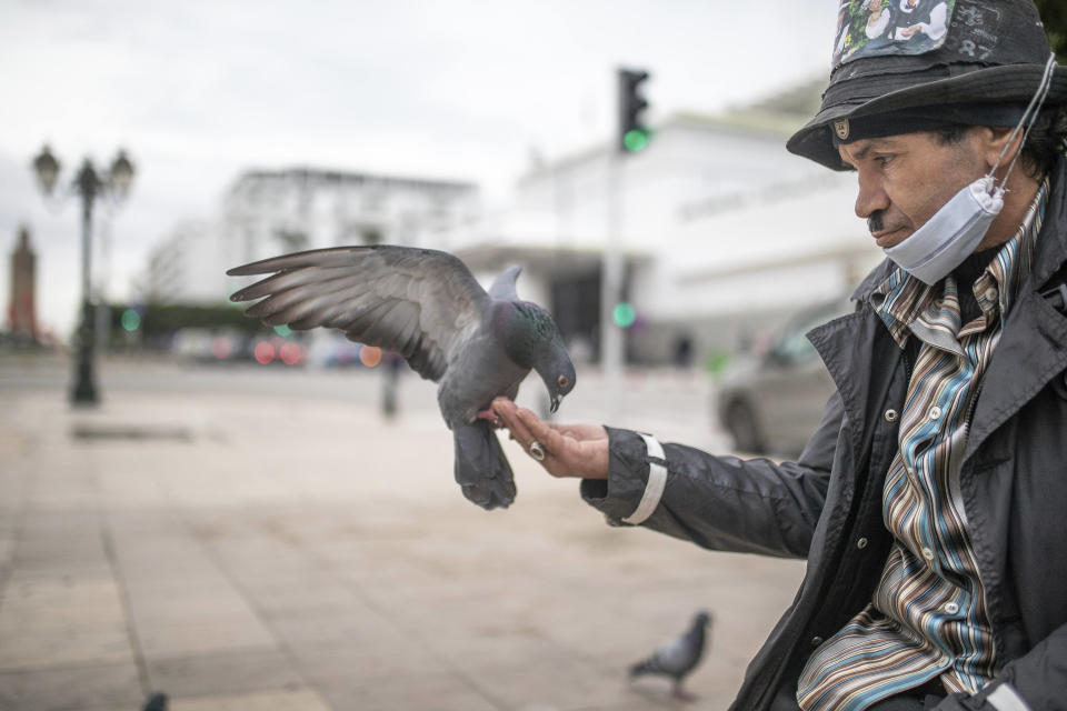 Belhussein Abdelsalam, 58, a Charlie Chaplin impersonator feeds pigeons as he waits for customers in one of the main avenues in Rabat, Morocco, Wednesday, Dec. 16, 2020. When 58-year-old Moroccan Belhussein Abdelsalam was arrested and lost his job three decades ago, he saw Charlie Chaplin on television and in that moment decided upon a new career: impersonating the British actor and silent movie maker remembered for his Little Tramp character. (AP Photo/Mosa'ab Elshamy)