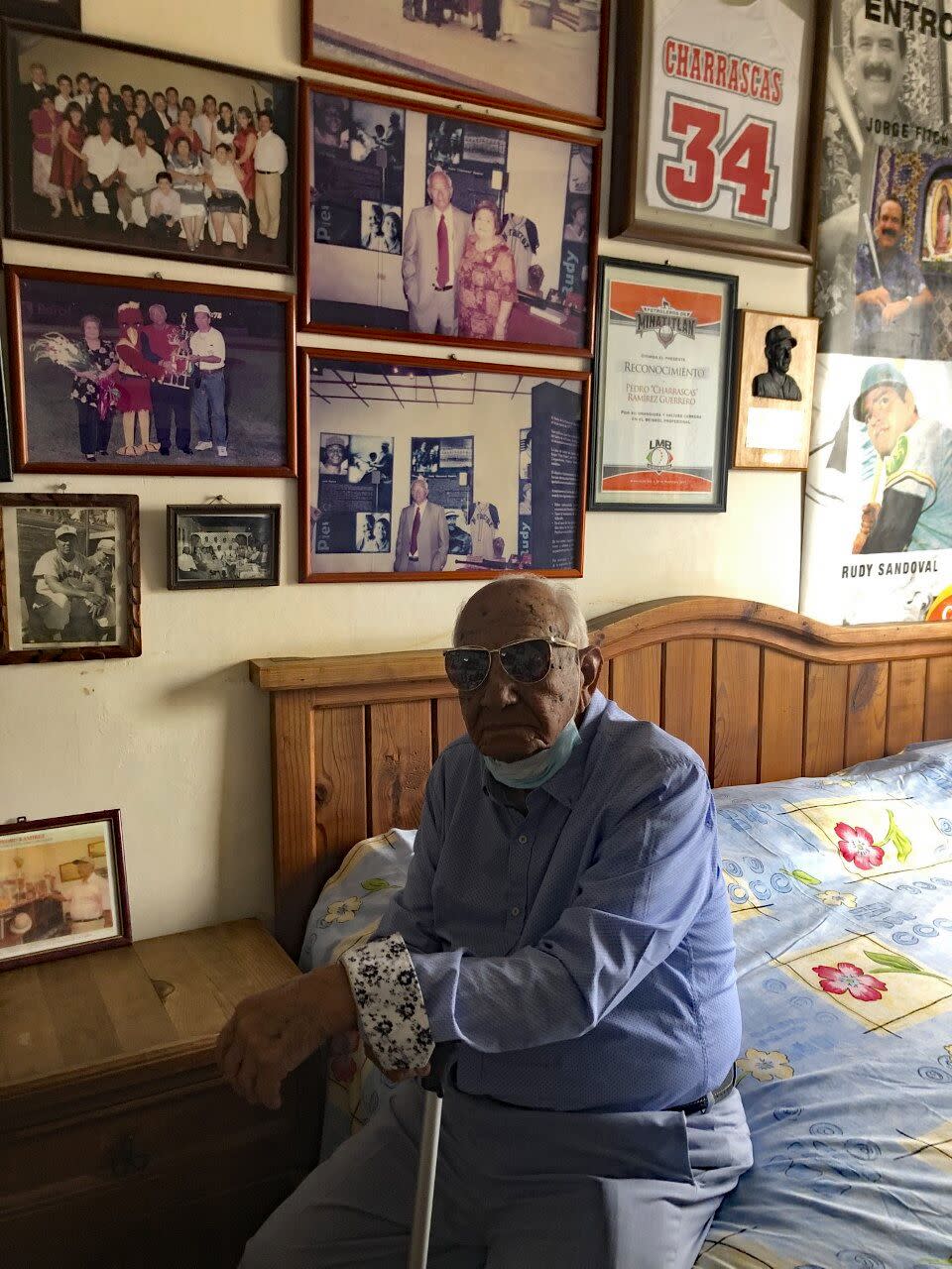 Pedro "Charrascas" Ramírez sits in his home next to photos of his family and baseball memorabilia. 2022.