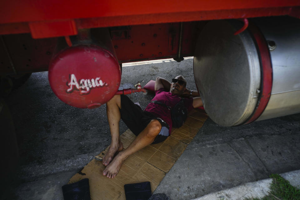 A farm worker sleeps under a truck while waiting in line to refuel his tractor, on the highway to Pinar del Rio, Guanajay, Cuba, Thursday, May 18, 2023. Cuba is in the midst of an acute fuel shortage that has drivers and farmers waiting in line for days or even weeks in order to fuel up their vehicles and tractors. (AP Photo/Ramon Espinosa)
