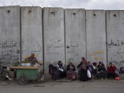 Palestinian women sit on a section of Israel's concrete separation barrier next to a small market at the West Bank city of Qalqilya, Wednesday, March 9, 2022. Twenty years after Israel decided to built its controversial separation barrier amid a wave of Palestinian attacks, it remains in place, even as Israel encourages its own citizens to settle on both sides and admits tens of thousands of Palestinian laborers. (AP Photo/Oded Balilty)