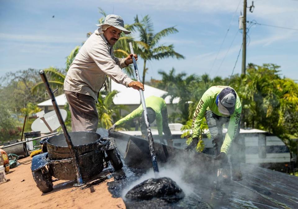 Gilberto Lujano, 49, left, spreads tar while working on a roof on Tuesday, May 2, 2023, in Homestead, Fla.