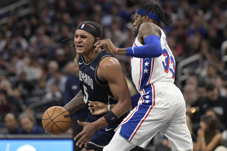 Orlando Magic forward Paolo Banchero (5) drives to the basket while defended by Philadelphia 76ers forward Robert Covington (33) during the first half of an NBA basketball game, Wednesday, Dec. 27, 2023, in Orlando, Fla. (AP Photo/Phelan M. Ebenhack)