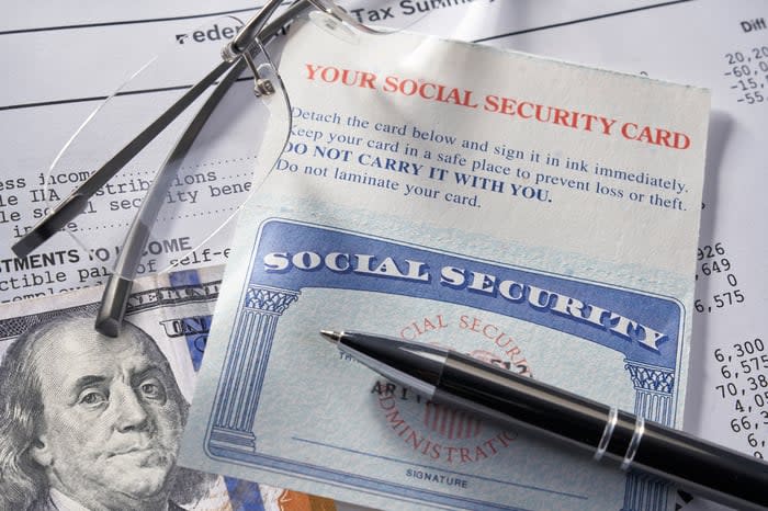 A Social Security card and a pen lying on papers and a $100 bill.