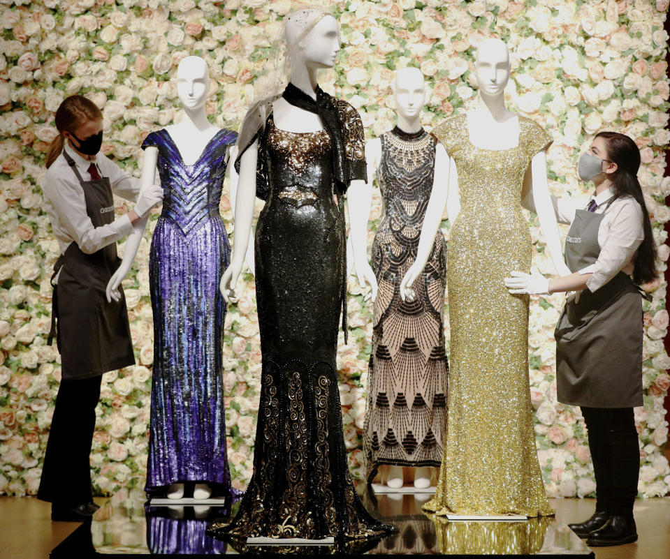 Gallery assistants handle a selection of dresses, including a gold sequined gown, right, worn by Penelope Cruz, amongst other items on display at Christie's, from the archive of fashion designer L'Wren Scott before it is offered at auction, in London, Thursday June 10, 2021. (Jonathan Brady/PA via AP)