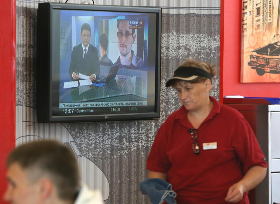 An airport worker passes a TV screen with a news program showing a report on Edward Snowden at Sheremetyevo,airport in Moscow Wednesday, June 26, 2013. Russia’s President Vladimir Putin said Tuesday that National Security Agency leaker Edward Snowden has remained in Sheremetyevo’s transit zone, but media that descended on the airport in the search for him couldn’t locate him there.(AP Photo/Sergei Grits)