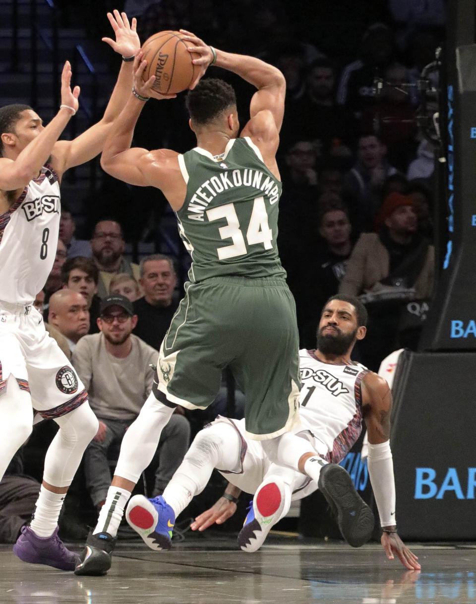 Brooklyn Nets guard Kyrie Irving (11), right, goes to the ground as Milwaukee Bucks forward Giannis Antetokounmpo (34) gets an offensive foul driving to the basket, during a NBA basketball game, Saturday Jan. 18, 2020 in New York. (AP Photo/Bebeto Matthews)