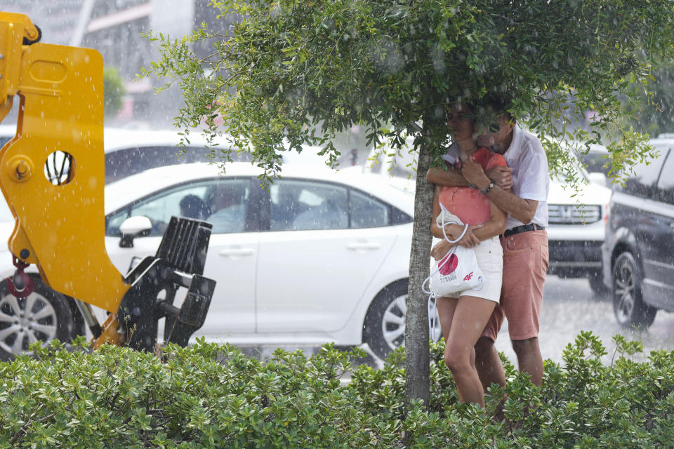 A couple attempts to shelter from a downpour as they wait outside the Florida Blue Training Facility in hopes of getting a glimpse of Lionel Messi leaving following a training session for the Inter Miami MLS soccer team Tuesday, July 18, 2023, in Fort Lauderdale, Fla.(AP Photo/Rebecca Blackwell)