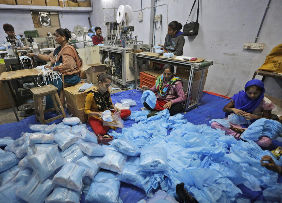 In this Saturday, Feb. 1, 2020, photo, Indian laborers work at a surgical mask production unit in Ahmadabad, India. India has banned the export of all varieties of respiratory masks in view of a viral outbreak that began in China which has infected more than 14,550 people globally. (AP Photo/Ajit Solanki)