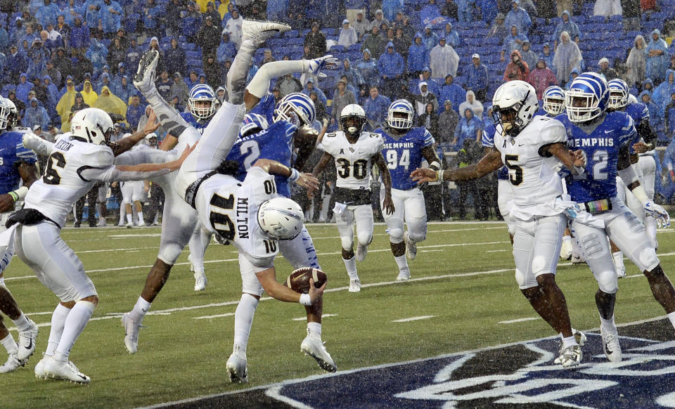 Central Florida quarterback McKenzie Milton (10) dives over Memphis defensive back's Josh Perry (4) and T.J. Carter (2) as he scores the go-ahead touchdown on a 7-yard run in the second half of an NCAA college football game Saturday, Oct. 13, 2018, in Memphis, Tenn. Central Florida won 31-30. (AP Photo/Mark Zaleski)