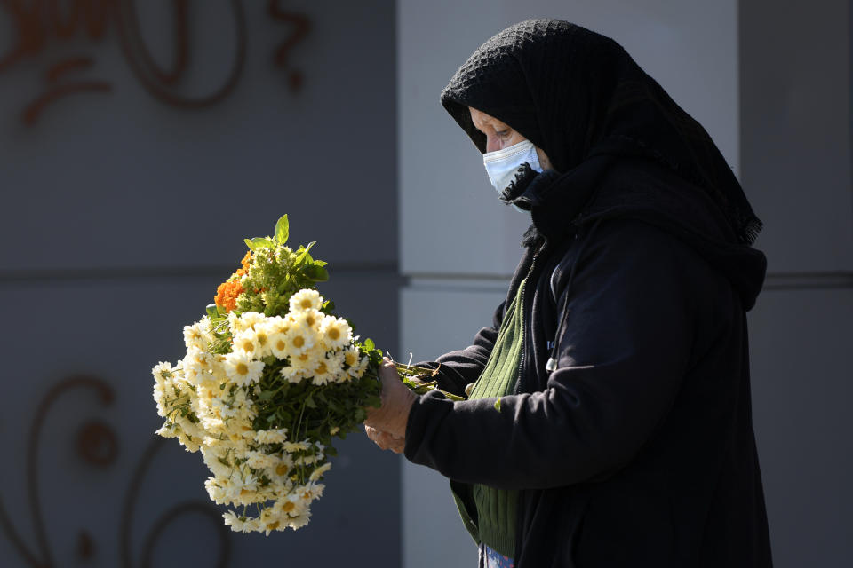 An elderly flower vendor wears a face mask for protection against COVID-19 infection in Bucharest, Tuesday, Oct. 20, 2020. Local authorities imposed the use of face masks in all public spaces, indoors and outdoors, closed schools, restaurants, theatres and cinemas after the rate of COVID-19 infections went above 3 cases per 1000 inhabitants in the Romanian capital Bucharest. (AP Photo/Andreea Alexandru)