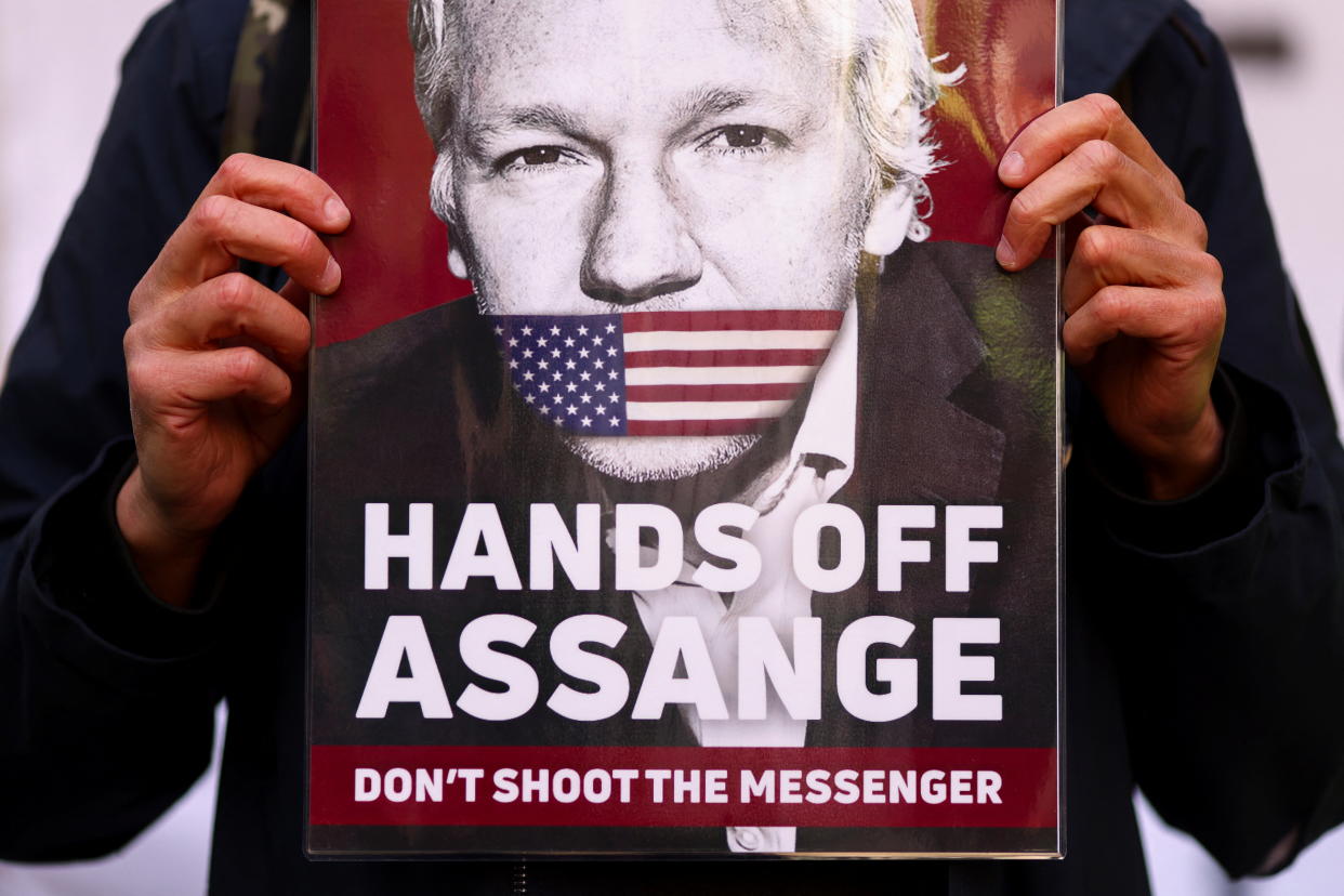 A Julian Assange supporter holds up a sign showing Assange's face with a U.S. flag over his mouth and the words: Hands Off Assange: Don't Shoot the Messenger.