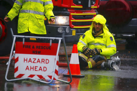 A fireman sits on a road holding a hose that is pumping water out of a residential block after it flooded due to heavy rain in Sydney, Australia, November 28, 2018. REUTERS/David Gray