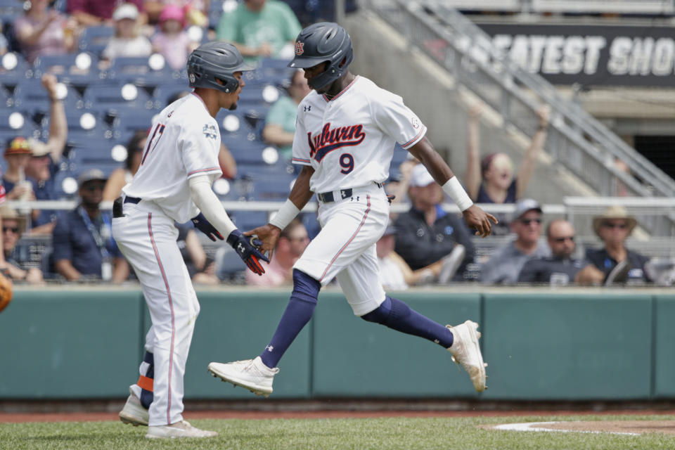 Auburn's Ryan Bliss (9) is greeted by Auburn's Will Holland, left, after he scored a run against Louisville on a double by Conor Davis in the seventh inning of an NCAA College World Series baseball game in Omaha, Neb., Wednesday, June 19, 2019. (AP Photo/Nati Harnik)