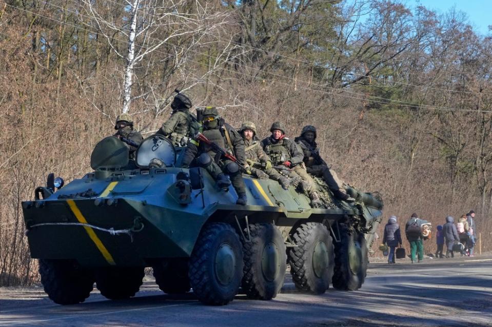 Ukrainian soldiers on an armoured personnel carrier pass by people carrying their belongings as they flee the conflict, in the Vyshgorod region close to Kyiv (AP)