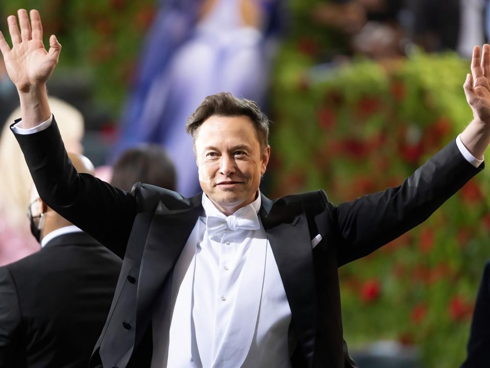 Elon Musk greets onlookers with both hands waving, at the 2022 Met Gala