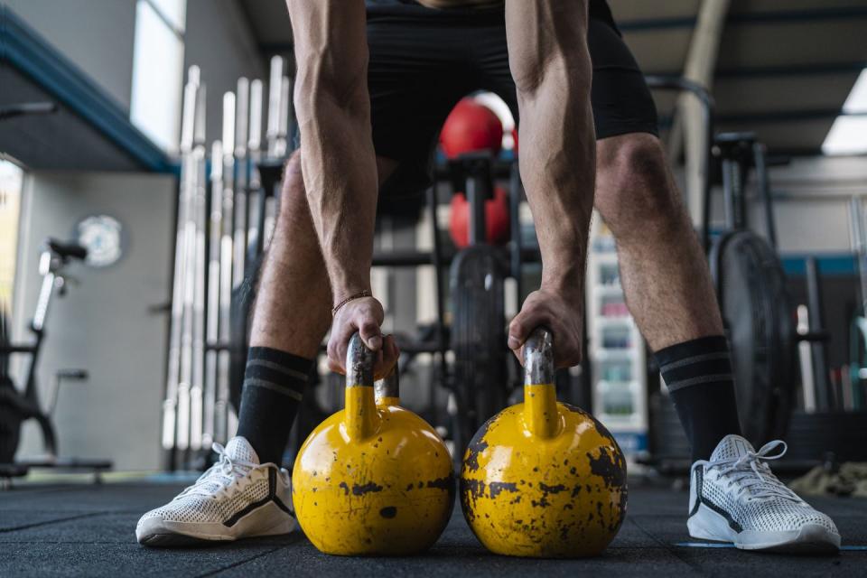 muscular male athlete holding kettlebells in gym