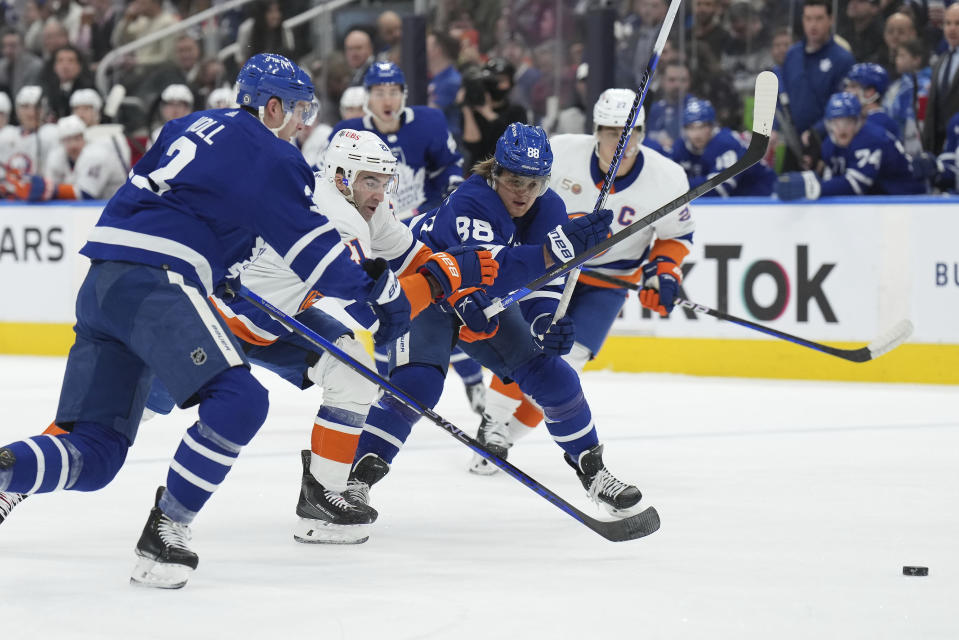 Toronto Maple Leafs defenseman Justin Holl (3), New York Islanders center Kyle Palmieri (21) and Maple Leafs right wing William Nylander (88) race toward the puck during first-period NHL hockey game action in Toronto, Ontario, Monday, Jan. 23, 2023. (Nathan Denette/The Canadian Press via AP)