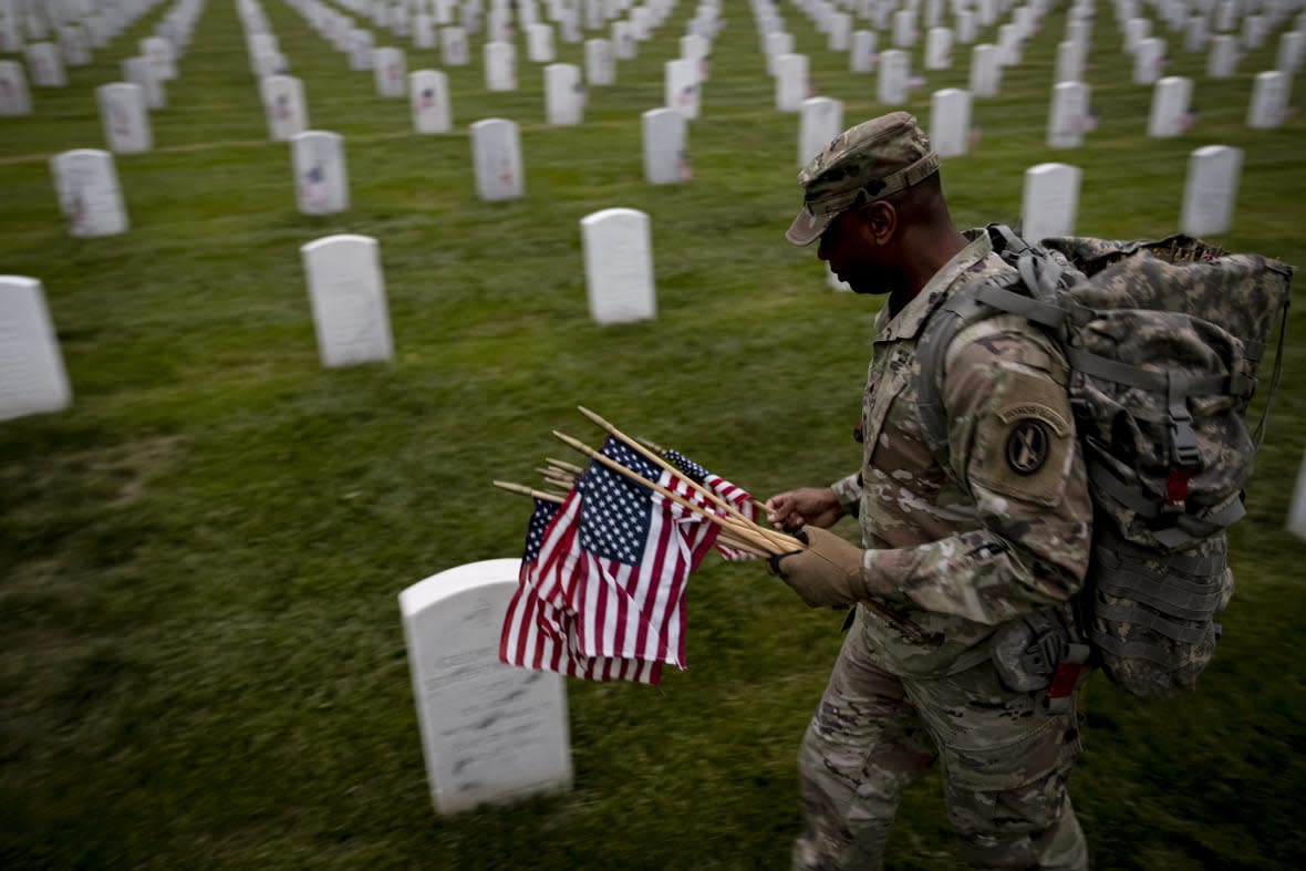 A member of the 3rd U.S. Infantry Regiment also known as The Old Guard, places flags in front of each headstone for “Flags-In” before sunrise at Arlington National Cemetery in Arlington, Thursday, May 25, 2023, to honor the Nation’s fallen military heroes ahead of Memorial Day. (AP Photo/Andrew Harnik)