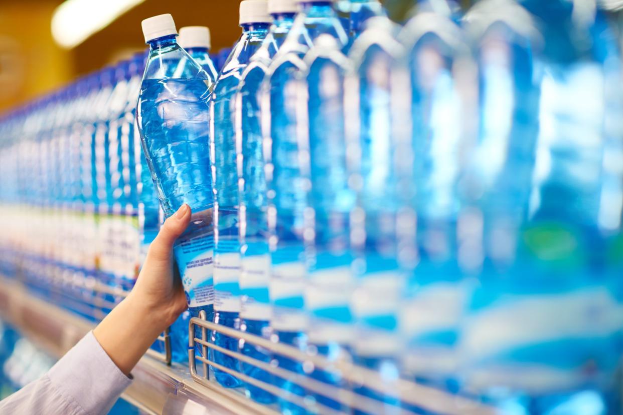 Hand taking bottle of mineral water from shelf in food store