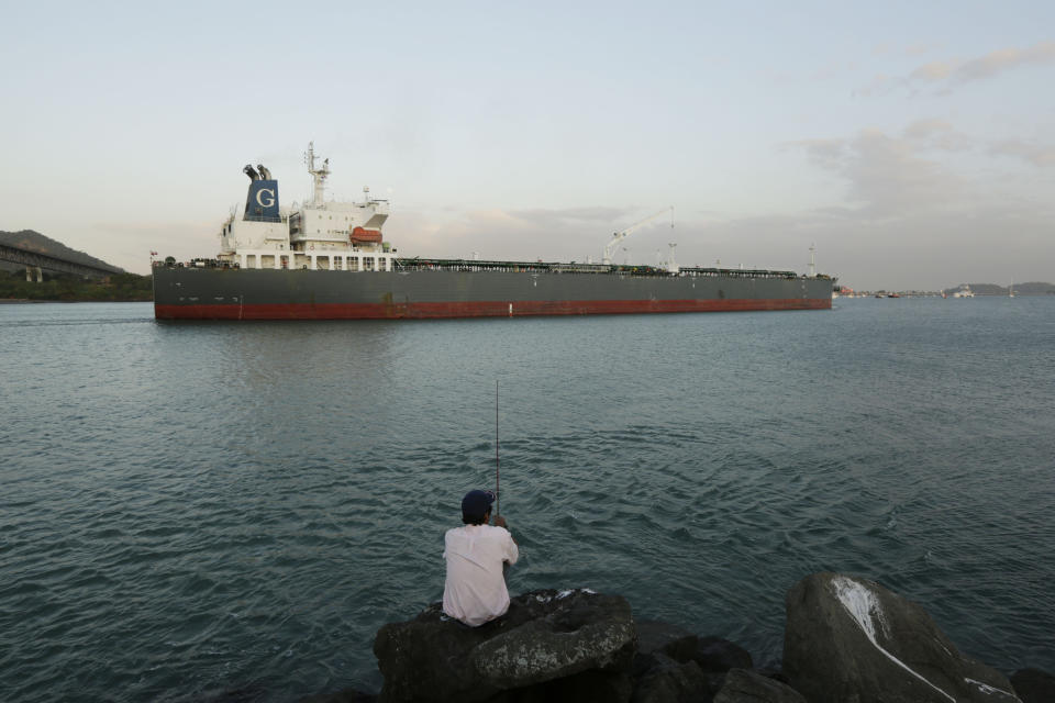 In this Jan. 14, 2014 photo, a man fishes where a cargo ship sails en route to the Pacific Ocean in Panama City. The Panama Canal is being expanded to accommodate a new generation of larger ships, known as post-Panamax, which have more than twice the carrying capacity of those able to pass through the canal today. But cost overruns are threatening a work stoppage on the canal's expansion. (AP Photo/Arnulfo Franco)