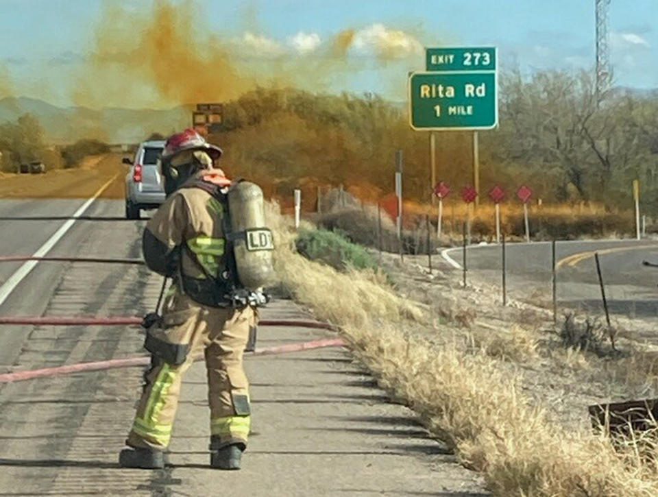 In this photo provided by the Tucson Fire Department, personnel work to control the hazardous material leak and brush fire incidents at Rita Rd. and Interstate 10 near Tucson, Ariz., Tuesday, Feb. 14, 2023. Officials in Arizona anticipate "an extended closure" of the state's main southern highway, a day after a deadly crash caused a hazardous material leak and forced evacuations nearby. (Tucson Fire Department via AP)