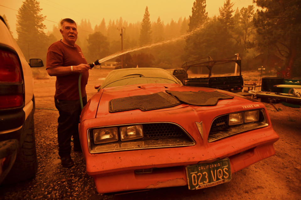 William Deal wets down his 1977 Trans Am as the Dixie Fire approaches Crescent Mills in Plumas County, Calif., Saturday, July 24, 2021. Deal, who lives in a community under evacuation orders, planned to stay to defend his home from the fire. (AP Photo/Noah Berger)