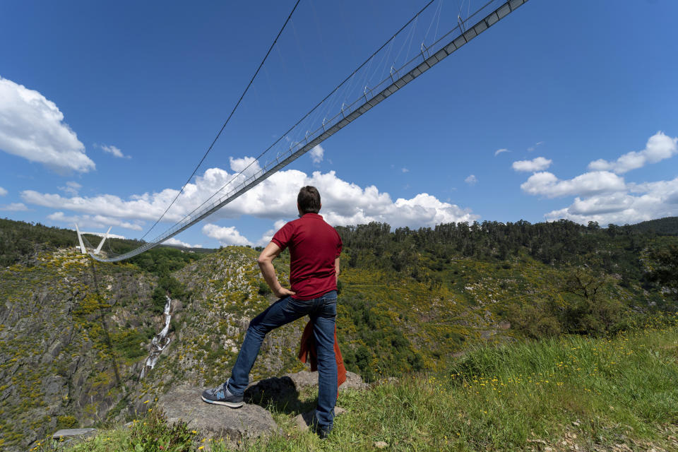 A man looks at a narrow footbridge suspended across a river canyon, which claims to be the world's longest pedestrian bridge, in Arouca, northern Portugal, Sunday, May 2, 2021. The Arouca Bridge inaugurated Sunday, offers a half-kilometer (almost 1,700-foot) walk across its span, some 175 meters (574 feet) above the River Paiva. (AP Photo/Sergio Azenha)