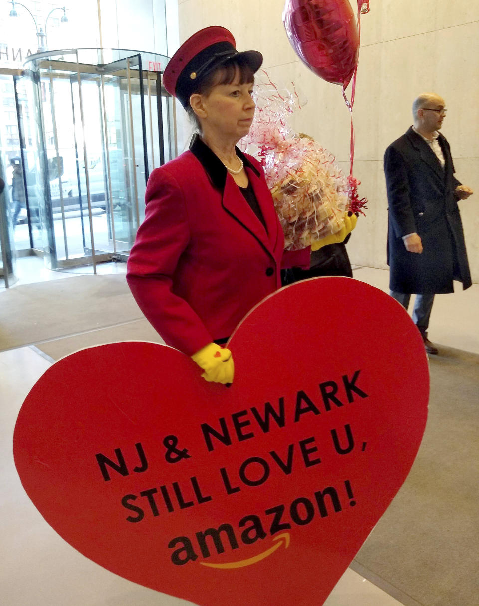 In this Feb. 14, 2019 photo provided by Newark Alliance, Laurie Ross, an actor with the event planners at Life 'O the Party, holds a message reading “NJ & Newark Still Love U, Amazon!” while arriving at an Amazon office in New York. The love note came despite Amazon saying it’s not seeking a new site. (Matthew Cossel/Winning Strategies for Newark Alliance via AP)