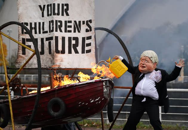 Performers from Ocean Rebellion dressed as U.K. Prime Minister Boris Johnson set light to the sail of a small boat which reads 