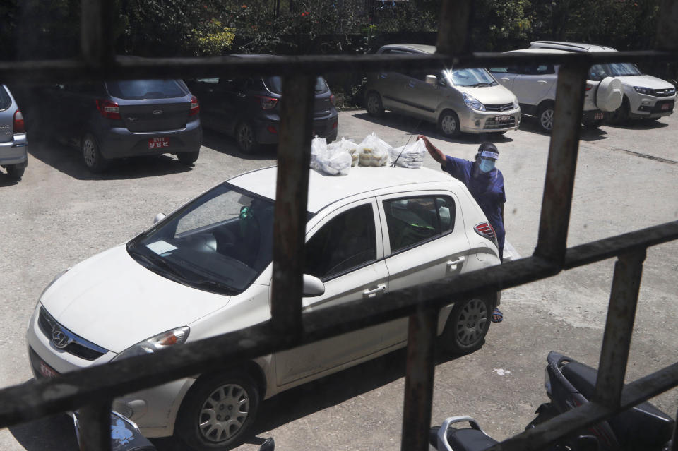 A nurse collects food for COVID-19 patients and health workers, placed on top of a car at Teaching hospital in Kathmandu, Nepal, Wednesday, Aug. 26, 2020. At one of the largest hospitals in Nepal, a pharmacist and taxi driver have teamed up to feed COVID-19 patients, doctors, nurses and health workers. Due to lockdowns, the cafeteria and nearby cafes have closed, leaving more than 200 staffers, patients and their families without food. The two friends have taken their own money and donations and put it to use buying groceries, renting a kitchen and paying helpers to provide the meals. (AP Photo/Niranjan Shrestha)