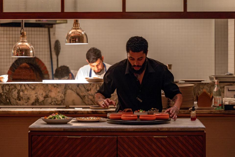 A man behind a counter, assembling a turntable of Lebanese platters of food.