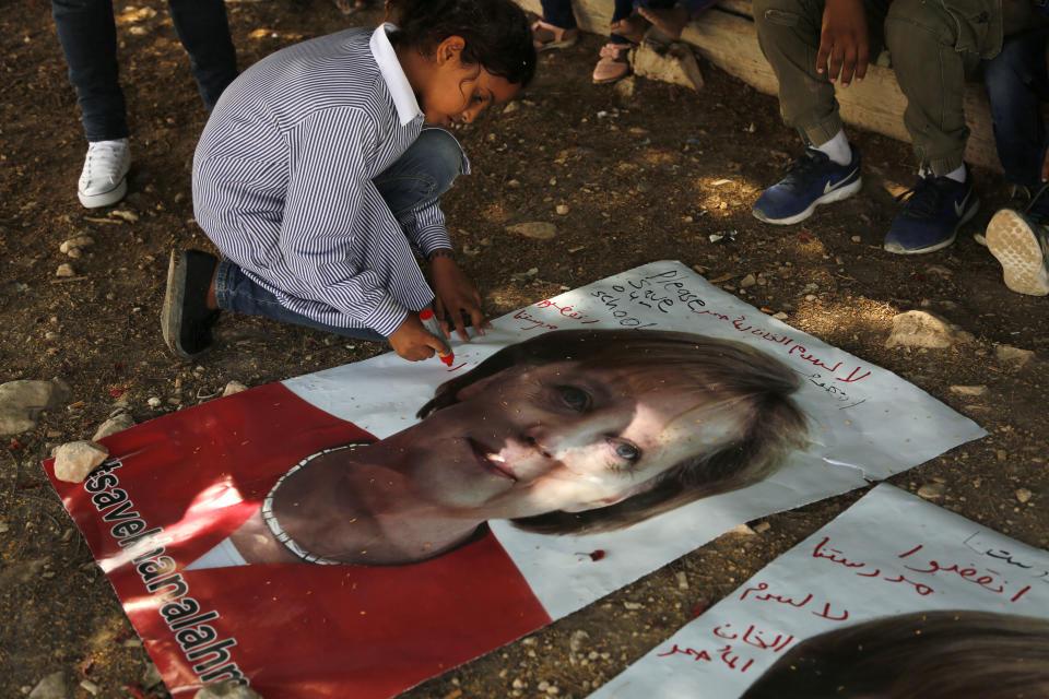 A Bedouin child writes on a picture of German Chancellor Angela Merkel ahead of her expected visit to Israel on Wednesday, in the West Bank Bedouin community of Khan al-Ahmar, Tuesday, Oct. 2, 2018. Children are pleading with Merkel to pressure Israel to halt demolition plans for the encampment of corrugated shacks outside an Israeli settlement east of Jerusalem. Arabic on the poster reads, "save Khan al-Ahmar" and "save our school." (AP Photo/Nasser Shiyoukhi)