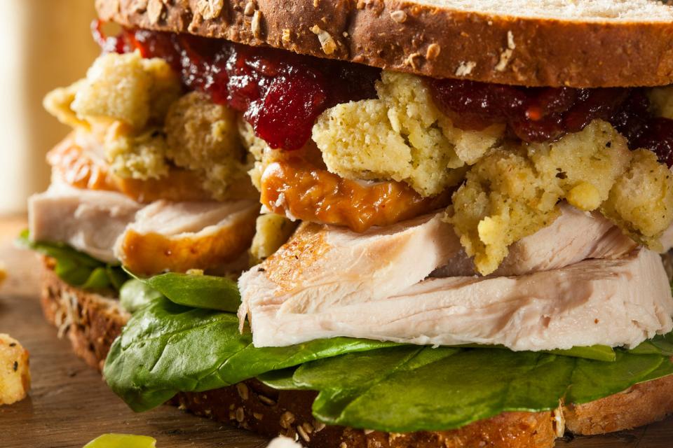 A close up of a leftover Thanksgiving turkey sandwich with stuffing, cranberry sauce, and whole grain bread.