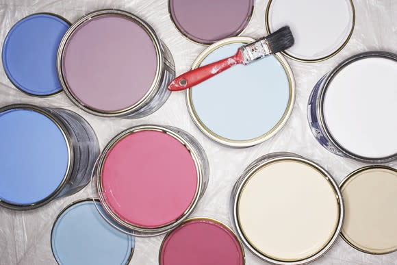 Cans filled with different colors of paint, with a red paint brush on top of one of them.