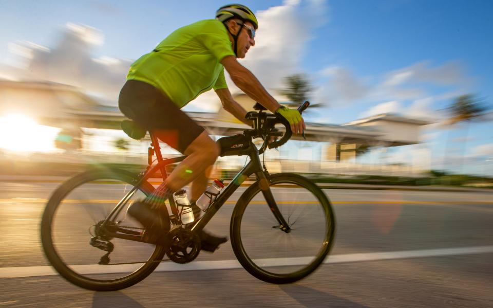 A cyclist rides southbound along South Ocean Boulevard near the Delray Beach Pavillioin at sunrise on June 28, 2022.