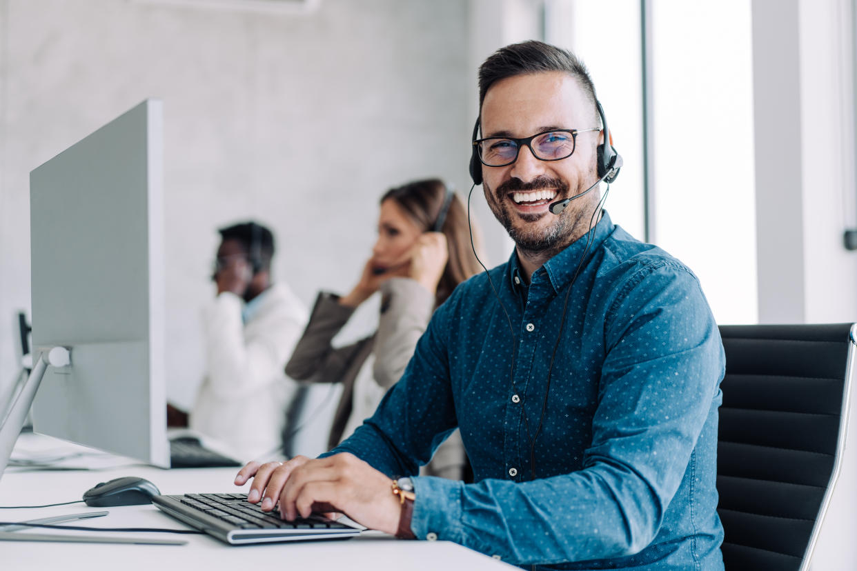 Shot of call center operators working in the office. Call center agent working with his colleagues in modern office. Smiling handsome businessman working in call center.